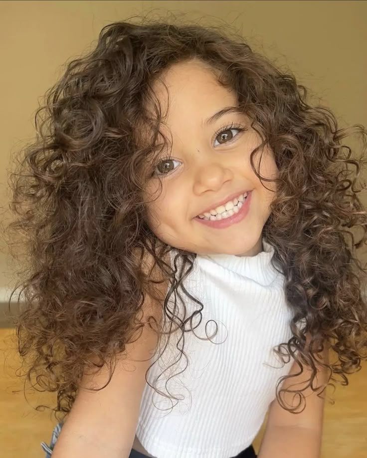 A smiling girl with full, evenly distributed curly hair framing her face.