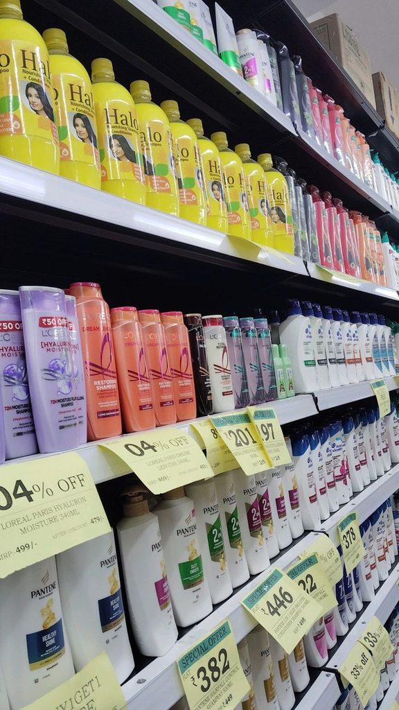 Rows of shampoo and conditioner bottles from different brands on store shelves with price tags."