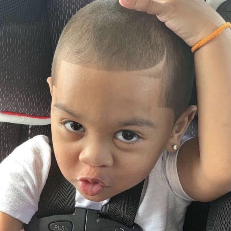 Close-up of a young boy in a car seat with a short buzz cut haircut, featuring a crisp, defined hairline along the front.
