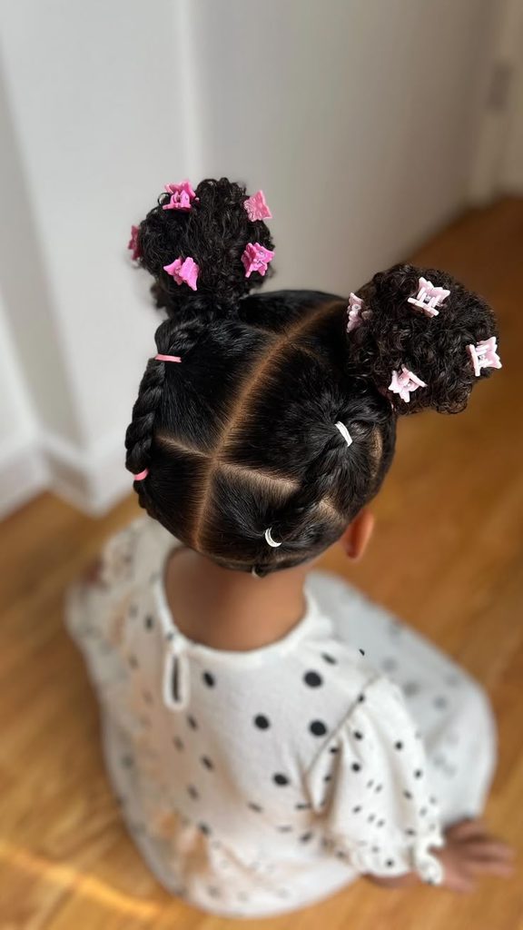Girl with curly hair styled into two sectioned puffs with pink bow clips
