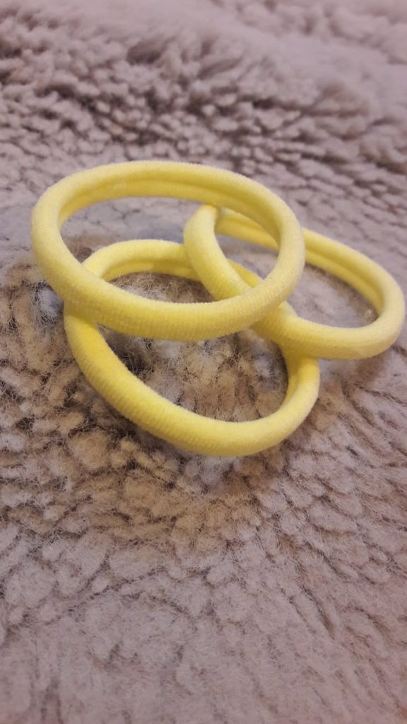hree soft yellow seamless hair ties on a textured fabric surface.