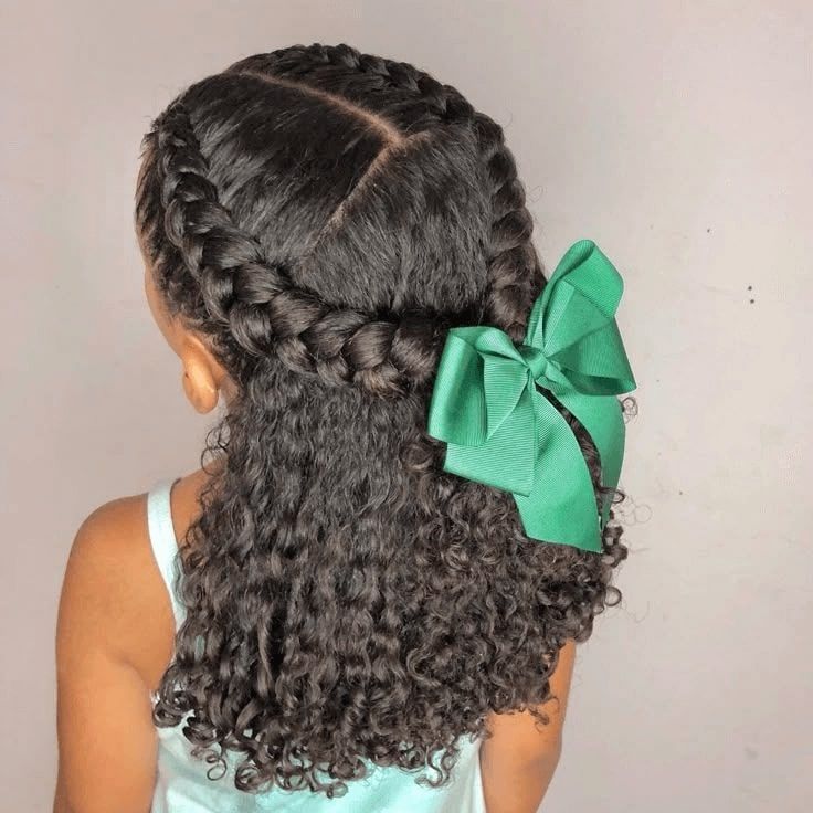 Girl with curly hair styled in a braided crown with a green bow.
