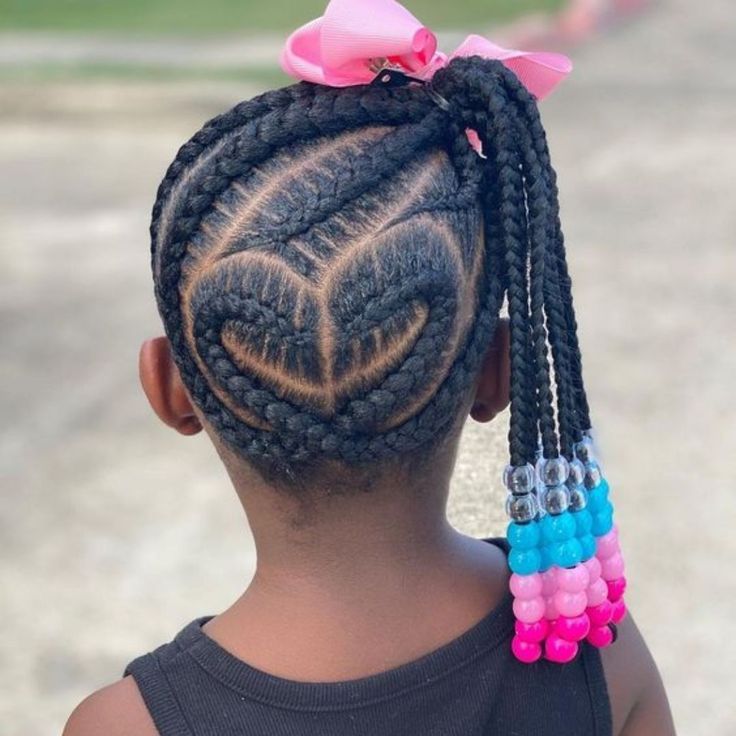 Young girl with heart-part cornrows leading into beaded braids, pink bow at the base