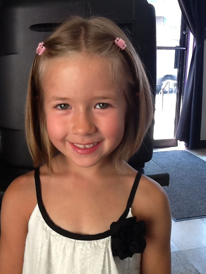 Young girl with a short straight bob, hair pinned back on both sides with small pink clips, smiling