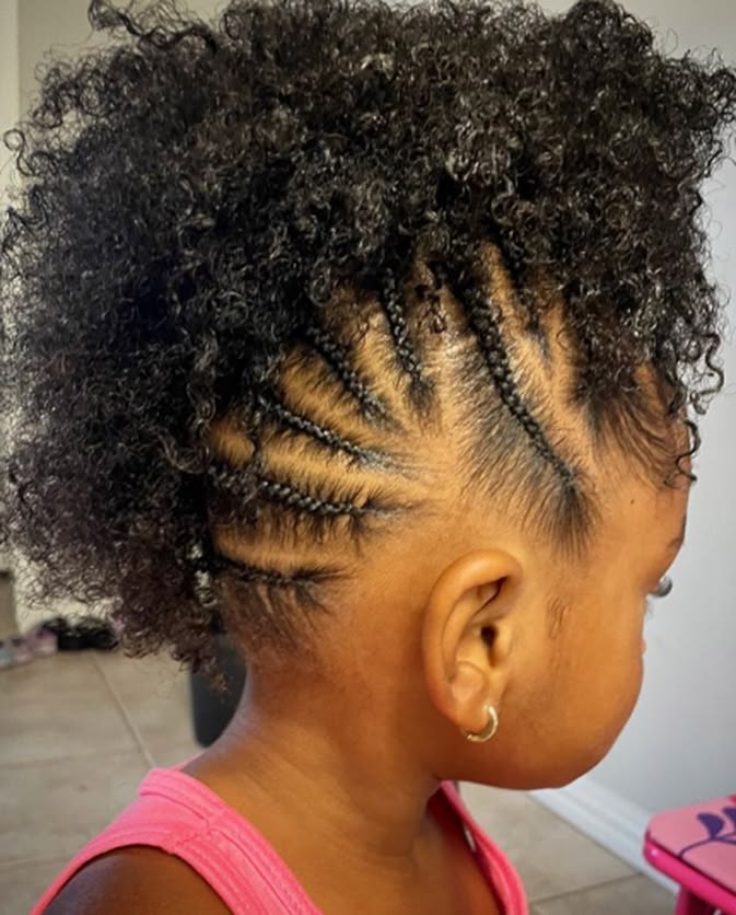 Young girl with a curly frohawk, cornrowed sides leading into a loose curly top, shown in profile