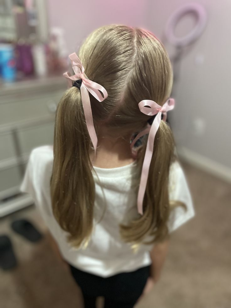 Girl with double low ponytails tied with pink ribbons.