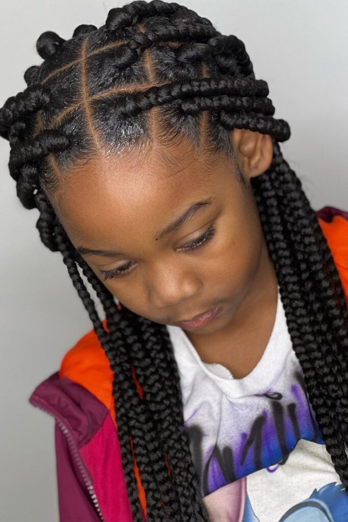Close-up of a child's box braids showing the square, crosshatch parting pattern at the scalp with thick, even braid