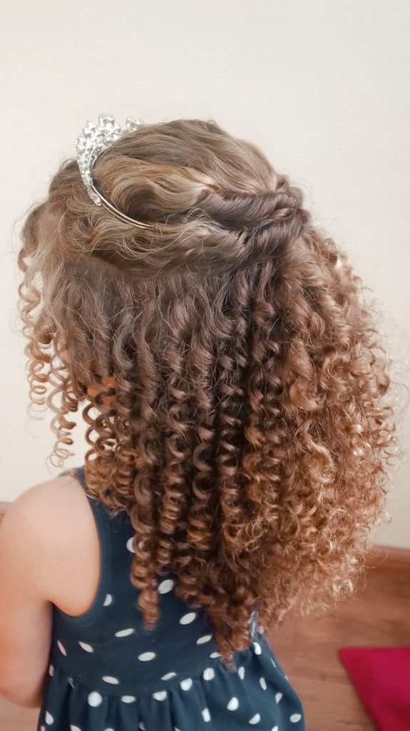 Young girl with a twisted curly crown and a rhinestone headband, loose curls cascading down her back