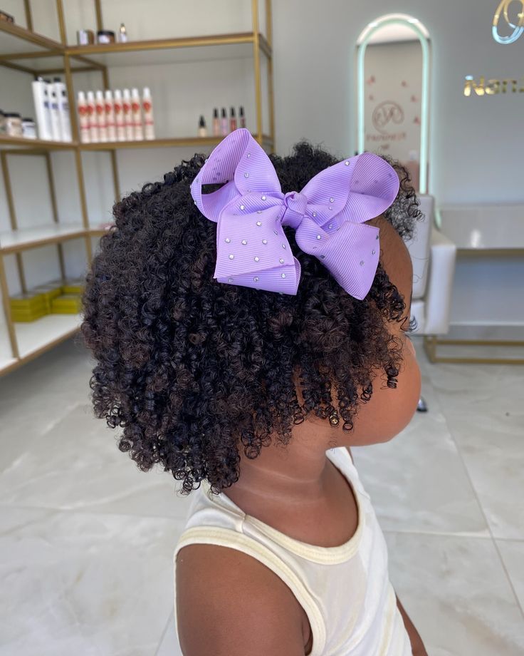 Young girl with a defined wash-and-go hairstyle and a lavender bow clipped near the top