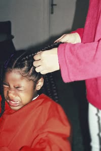 Child wincing while an adult braids her hair.