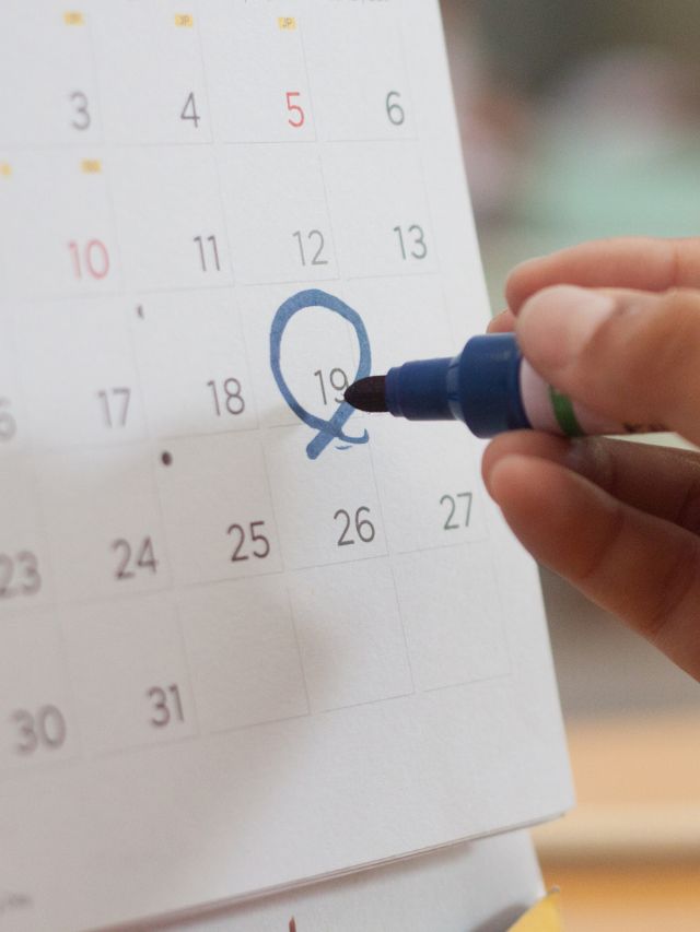 Hand circling a date on a wall calendar with a blue marker