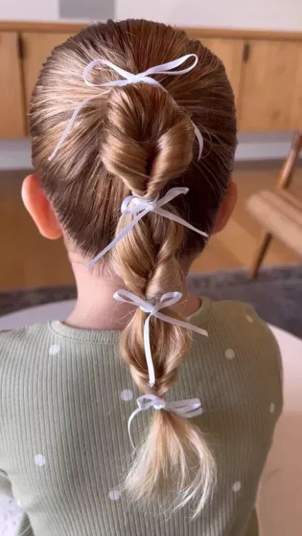 Young girl with a bubble ponytail sectioned with white ribbons, shown from behind