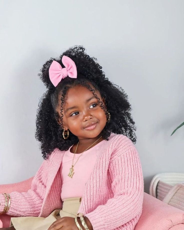 Young girl with curly hair half-up in a pink bow, loose curls framing her face