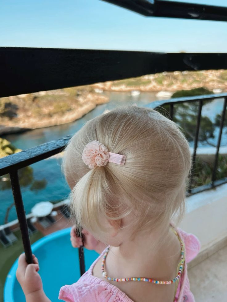 Toddler on a balcony with a side ponytail and flower clip
