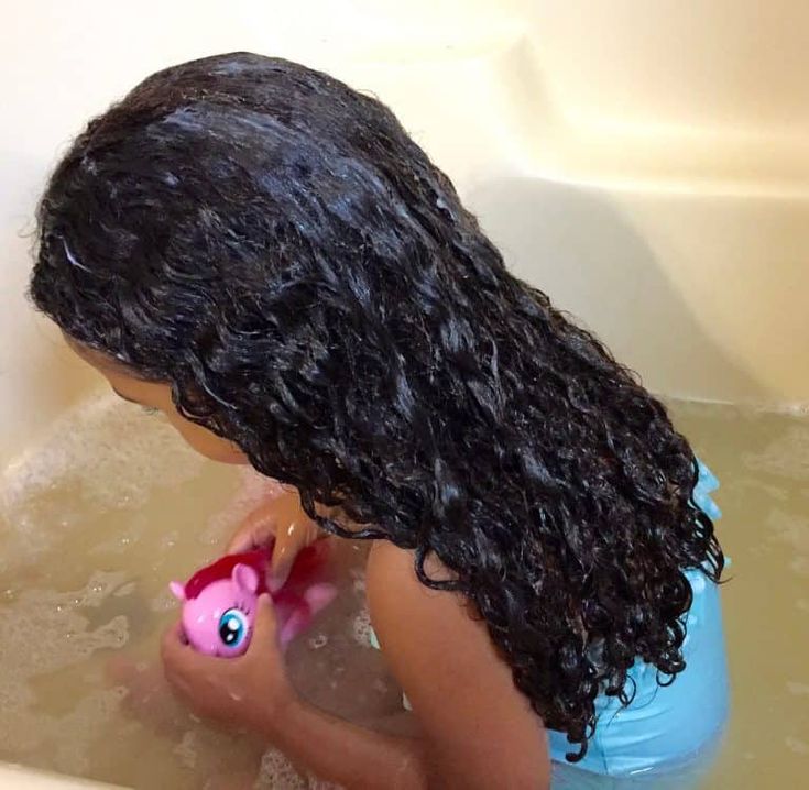 Child rinsing curly hair in the bath