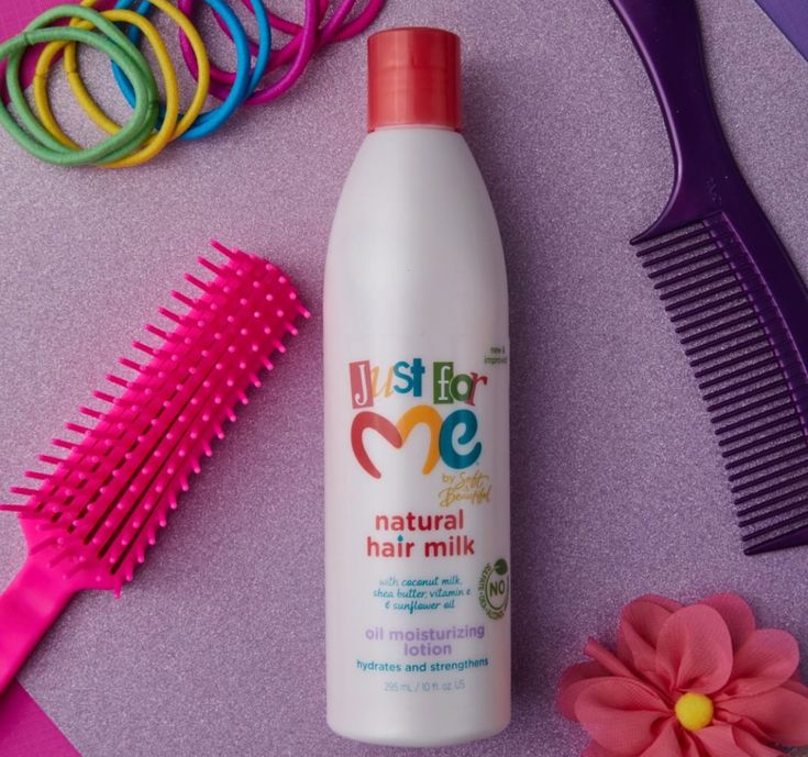 Bottle of Just For Me Natural Hair Milk surrounded by colorful hair ties, a pink brush, and a purple comb
