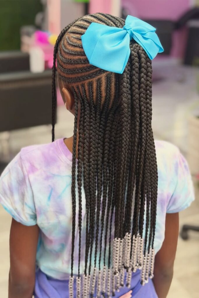 Little girl with feed-in cornrows transitioning into long box braids with silver beads, finished with a light blue bow