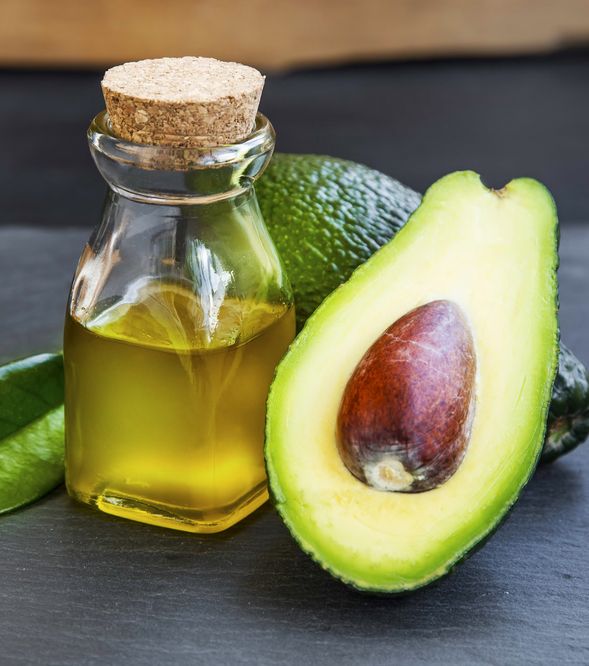 Bottle of avocado oil beside two avocado halves