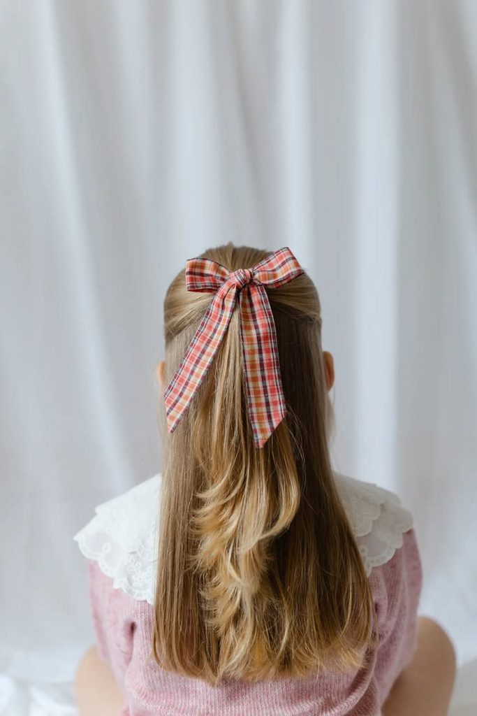 "Girl with a half-up hairstyle secured by a plaid bow, hair left down.
