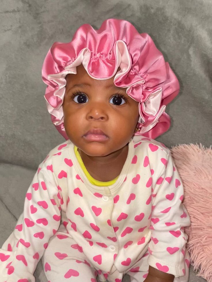 Baby wearing a pink satin bonnet, sitting on a couch