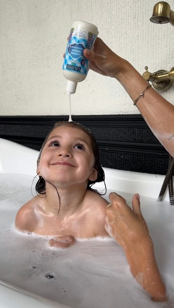 Parent applying shampoo to child's hair in the bath