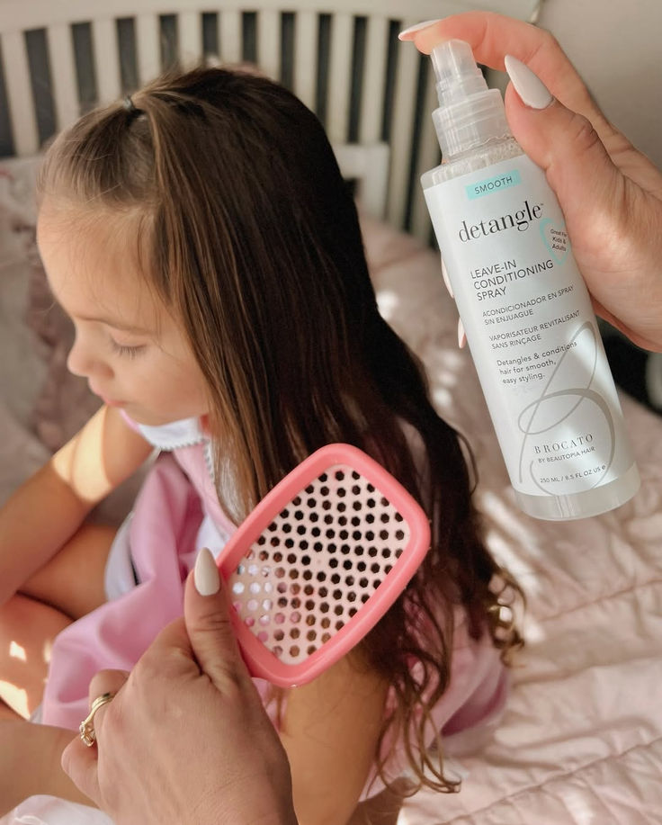 Parent applying leave-in conditioning spray to a child's hair before brushing