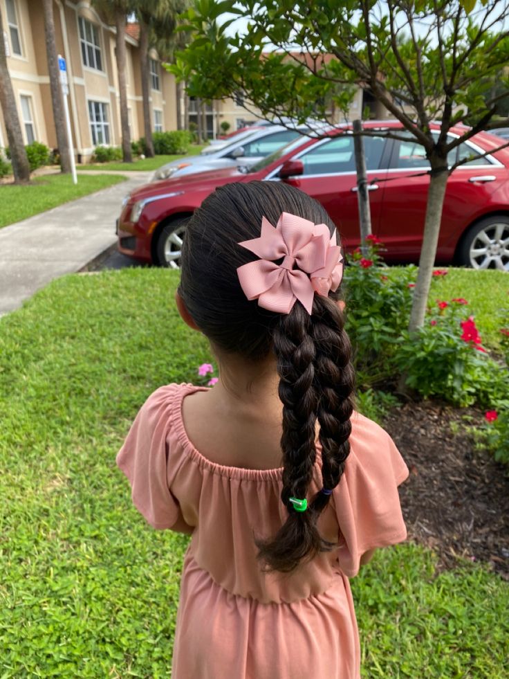 A child with 2 side braids draped over her shoulder with bows
