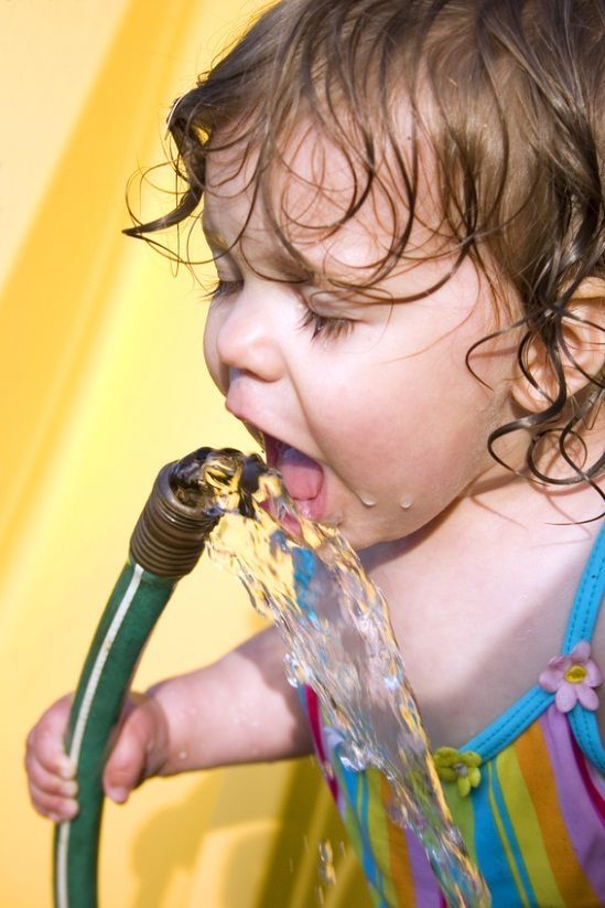 Child drinking water from a garden hose
