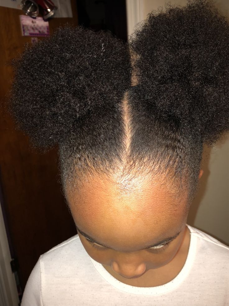 Child with hair styled into two natural curly puffs, showing a visible middle part.