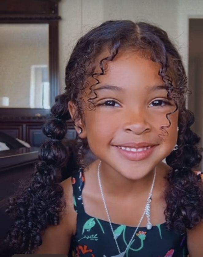 "Smiling little girl with curly hair styled in two pigtails
