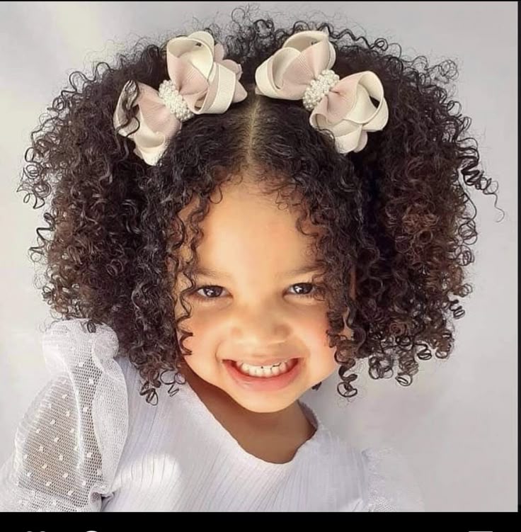 Smiling little girl with curly hair styled with two bows