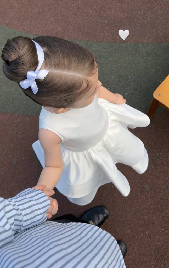 Toddler with hair in a smooth top bun tied with a white ribbon