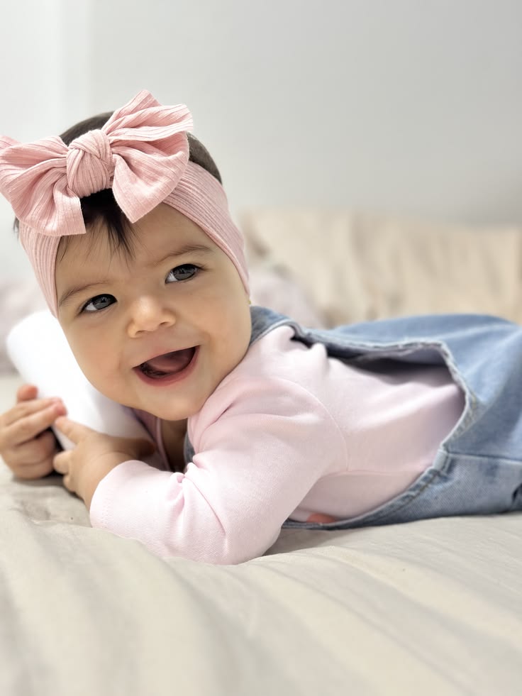 Baby wearing a pink bow headband, smiling on a bed