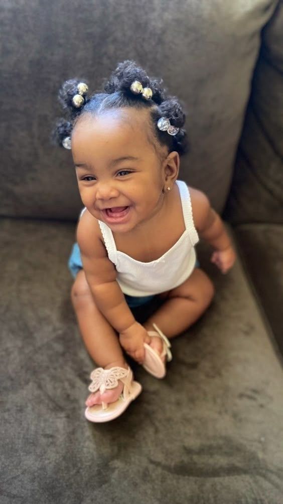 Toddler smiling with hair styled into small sectioned puffs with beaded ties