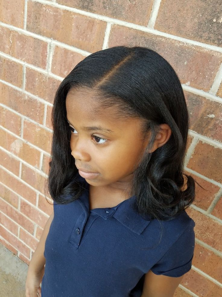 Young girl with medium-length straight hair and flipped-out ends, standing against a brick wall