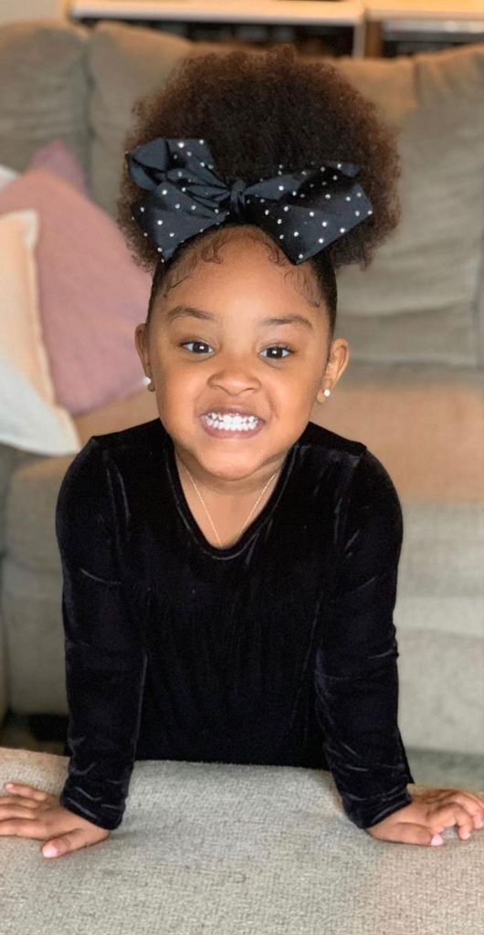 Young girl with a high afro puff and a black satin bow, smiling