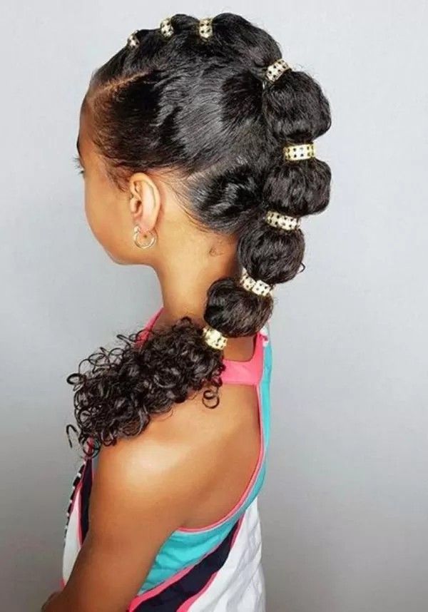 Young girl with a mohawk bubble ponytail, gold cuffs sectioning the hair into bubbles with curls at the end, shown in profile
