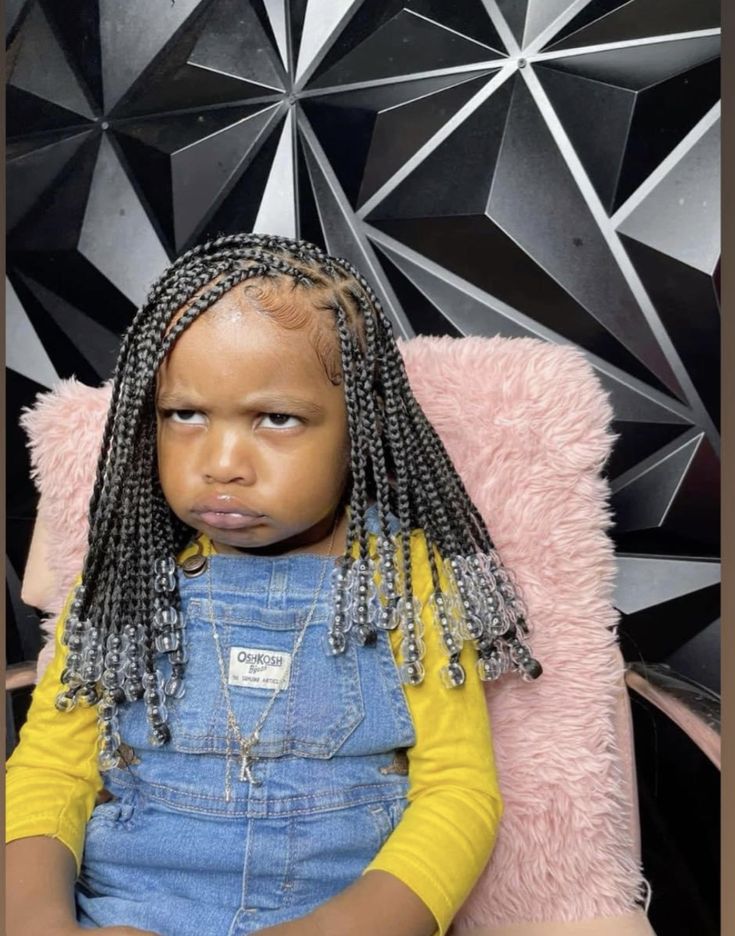 Young girl with box braids and clear beaded ends, sitting for a portrait