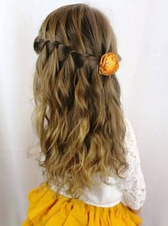Girl with a waterfall braid over loose wavy hair, accented with a flower clip.