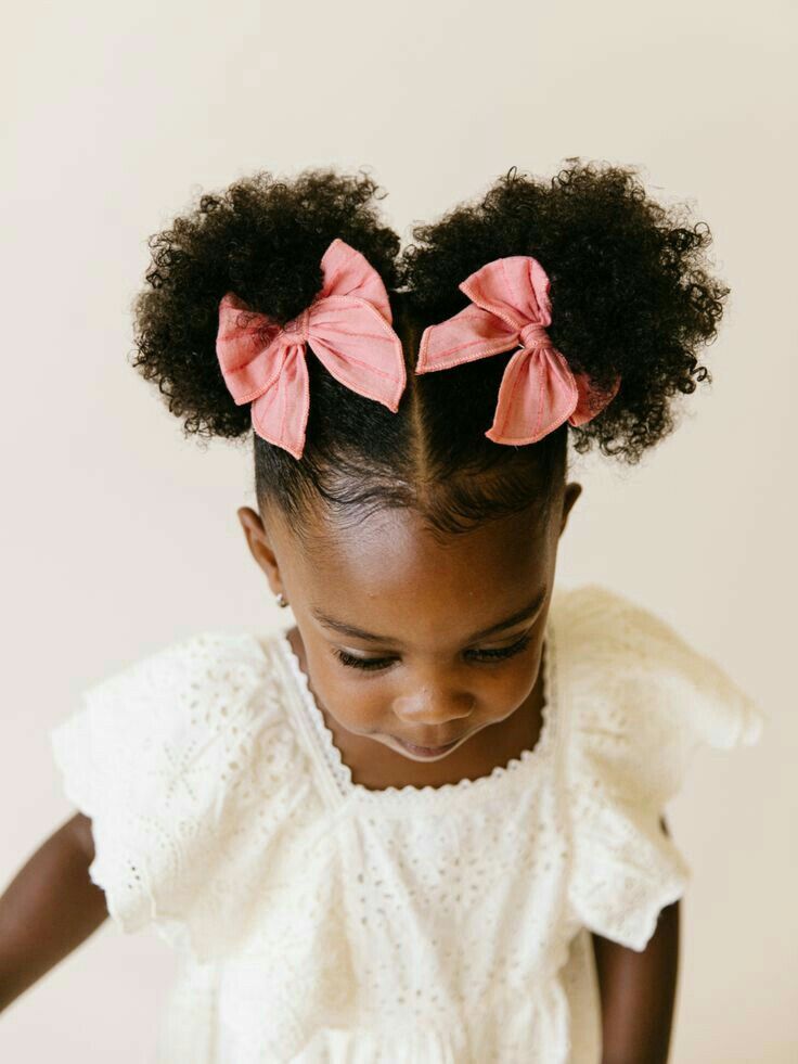 Girl with two afro puffs tied with coral bows.