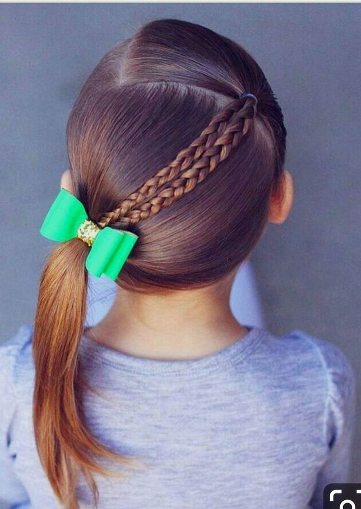 Girl with a low side ponytail and two thin braids running across her head, tied with a green bow