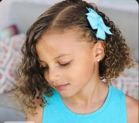 Young girl with a curly bob and a small blue bow pinned near the part