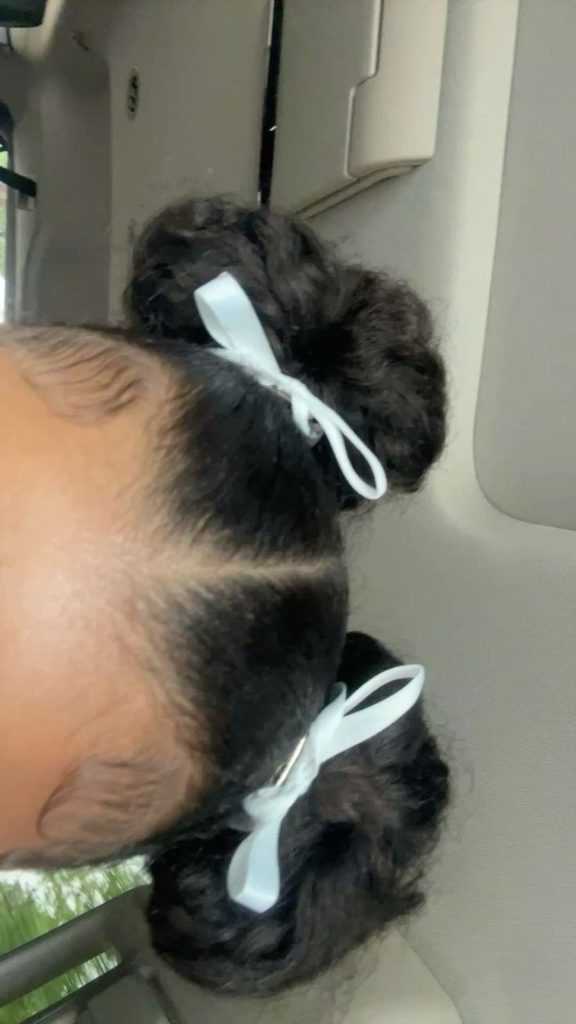 Young girl with two curly space buns, each wrapped with a white ribbon