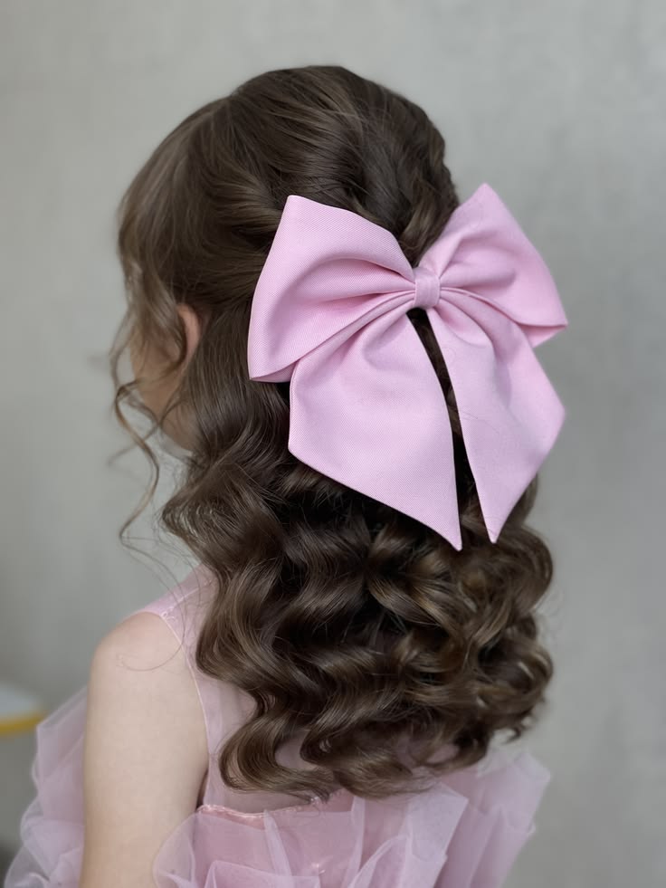 Young girl with a half-up hairstyle and a large pink bow, long curls flowing down her back