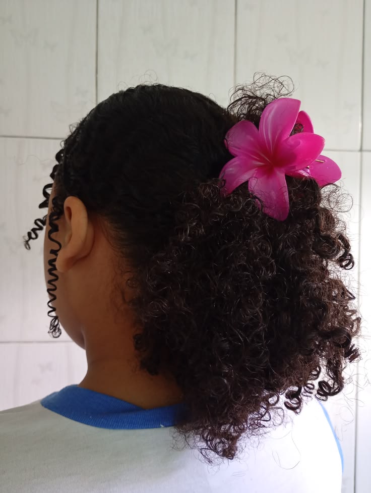 Young girl with a low curly ponytail and a bright pink flower clip at the base